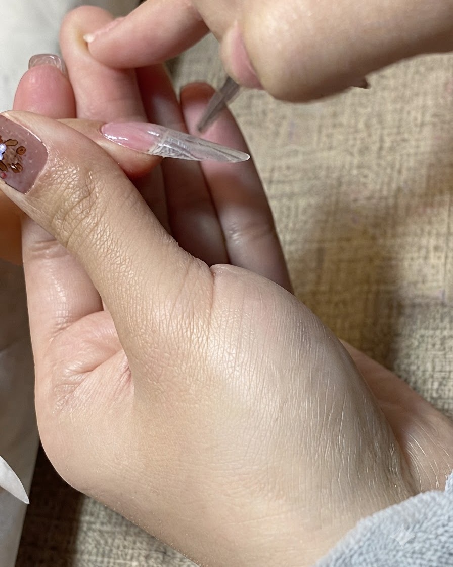 Un primo piano di un pennello di precisione che leviga il gel trasparente sulla superficie di unestensione per unghie.