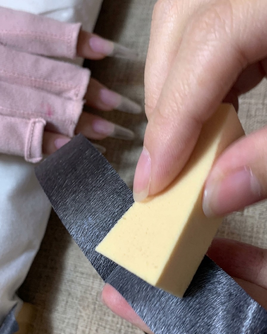 Una persona usa del nastro adesivo nero per pulire la polvere da una spugnetta triangolare gialla per il trucco.