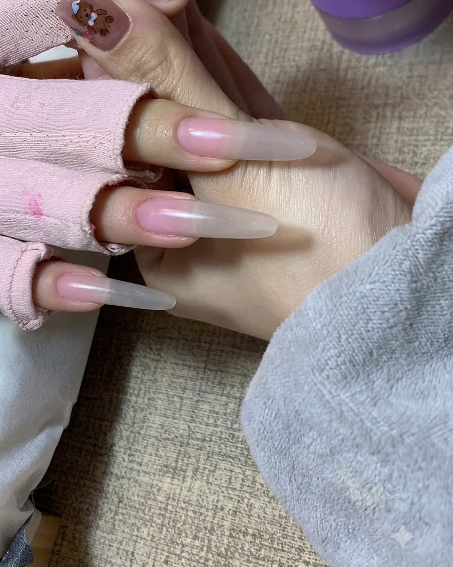 Una mano che tiene quella di una cliente mostrando un morbido effetto sfumato nude applicato con una spugnetta sulle estensioni delle unghie.
