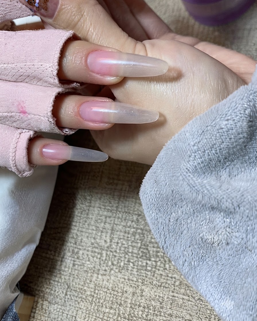 Primo piano di una mano che riceve il secondo strato di gel nude tamponato con cura sul margine libero.