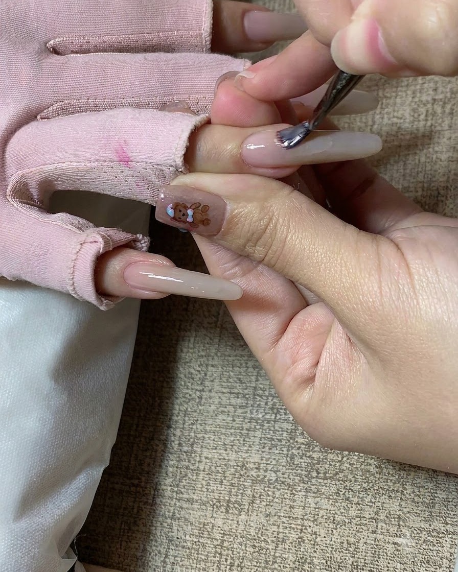 Un pennello per unghie che applica del gel color milk tea su ununghia lunga scolpita.