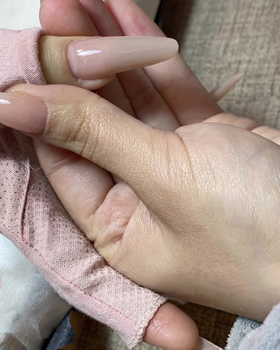 Primo piano di una mano che mostra ununghia con manicure color milk tea finita.