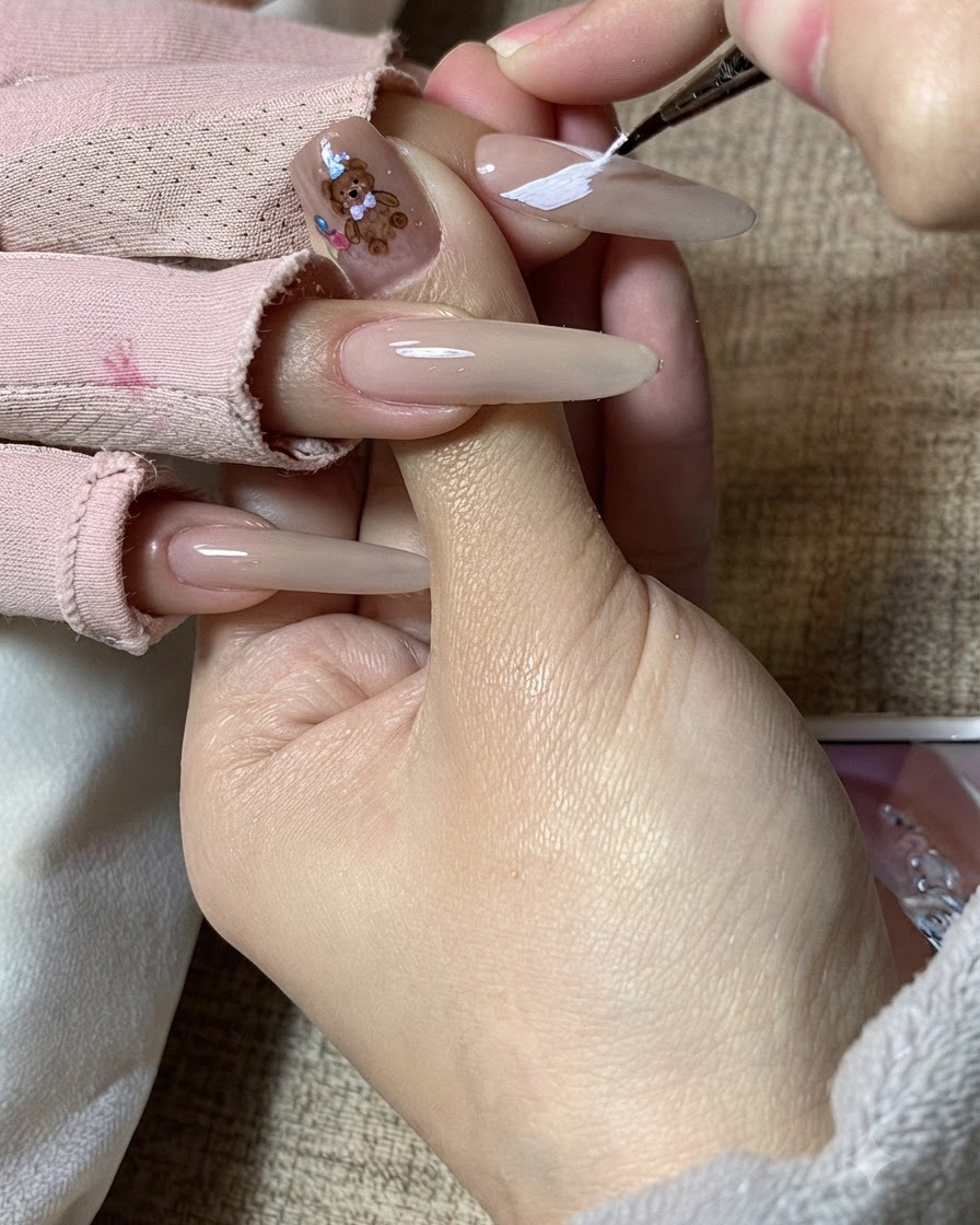 La mano di una nail artist che perfeziona i motivi bianchi delle ali di farfalla su ununghia allungata.