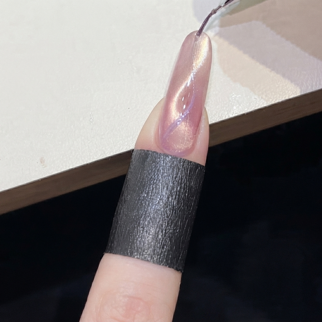 Un magnete cilindrico tenuto vicino a una linea cat-eye viola su ununghia rosa brillante.