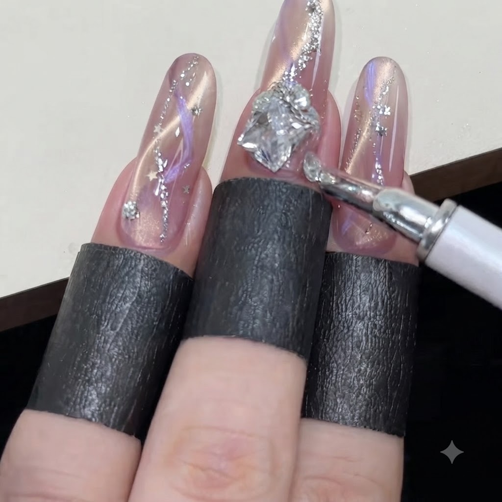 Una penna in cera che dispone piccoli strass rotondi attorno a una gemma più grande a forma di diamante su ununghia frizzante con cat-eye rosa.