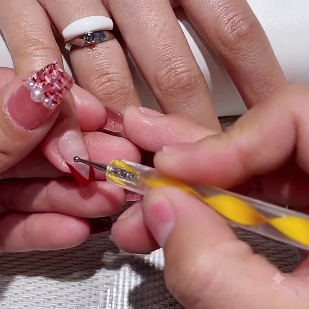 Un dotting tool con manico giallo che posiziona due piccoli punti rossi nello spazio negativo trasparente di ununghia con french a V.