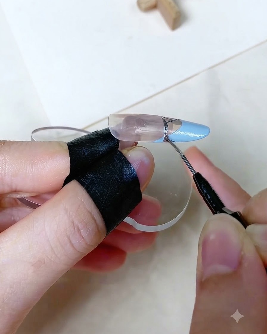 Una vista ravvicinata di un pennello da dettaglio fine che disegna una precisa linea metallica argentata sulla transizione di una French tip baby blue su un dito esositivo artificiale.