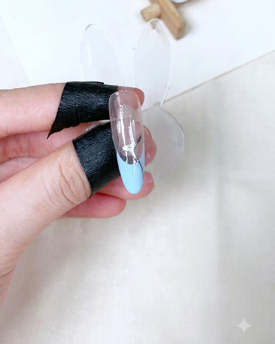 Un singolo supporto per unghie scolpite che mostra un top coat trasparente lucido polimerizzato con dettagli argentati su una French tip baby blue.