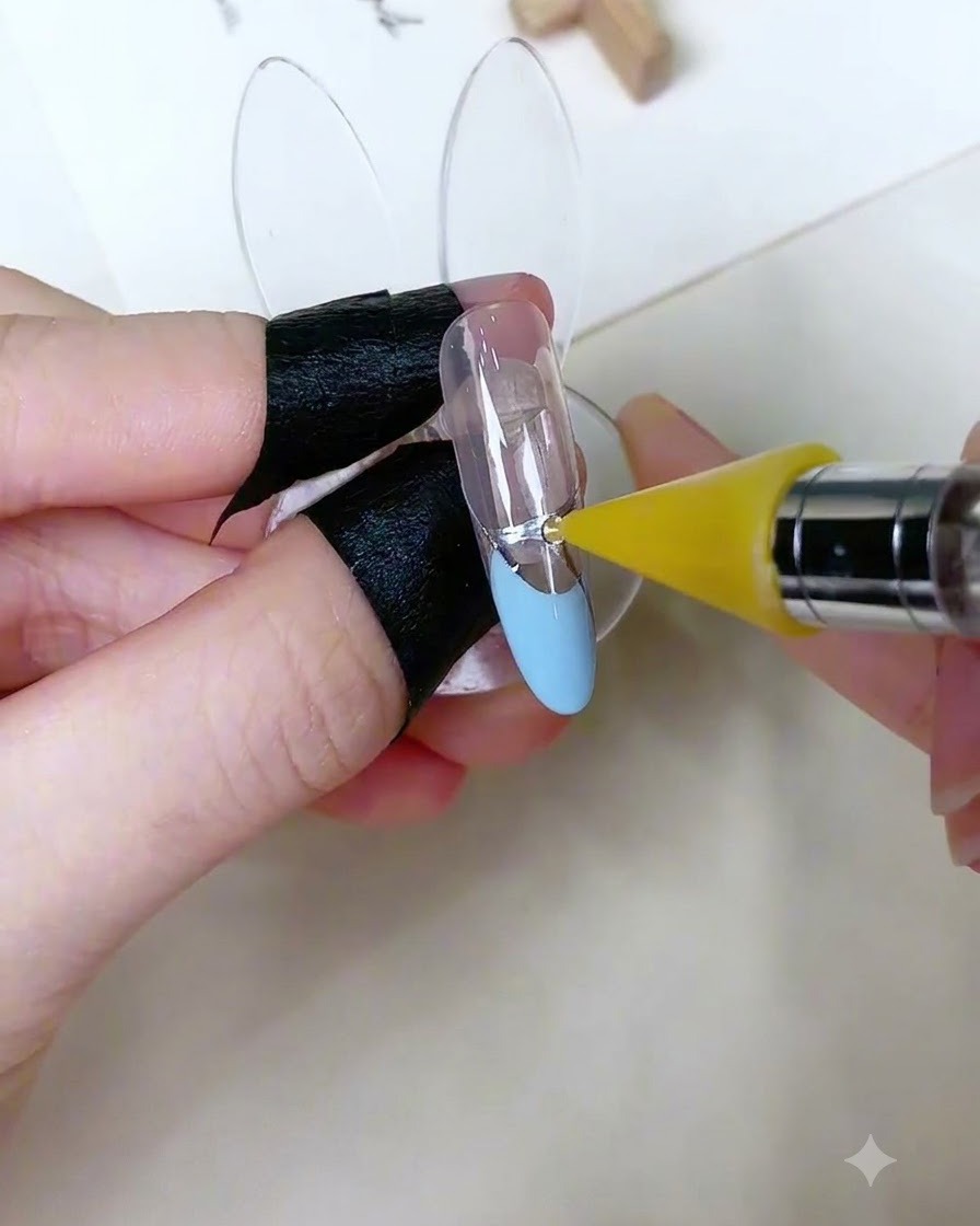 Uno strumento di prelievo specializzato che posiziona un piccolo strass rotondo su un punto di gel adesivo su ununghia decorata.