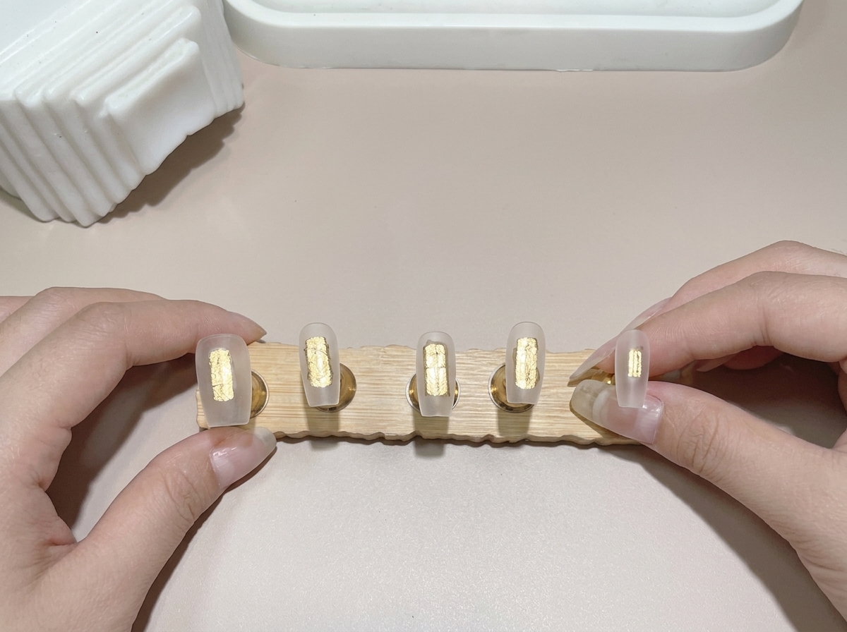 Primo piano di un pennello che applica la base gel su diverse tip montate su un espositore in legno.