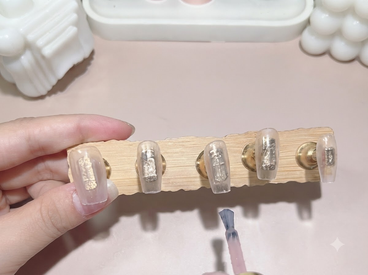 Un pennello stende un secondo strato di smalto rosa lattiginoso traslucido sulle tip fissate allespositore.