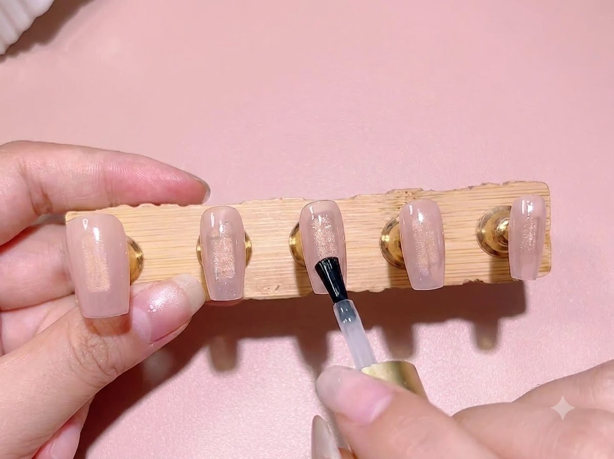 Un pennello stende uno strato di blooming gel trasparente sopra la base rosa traslucida di una tip.