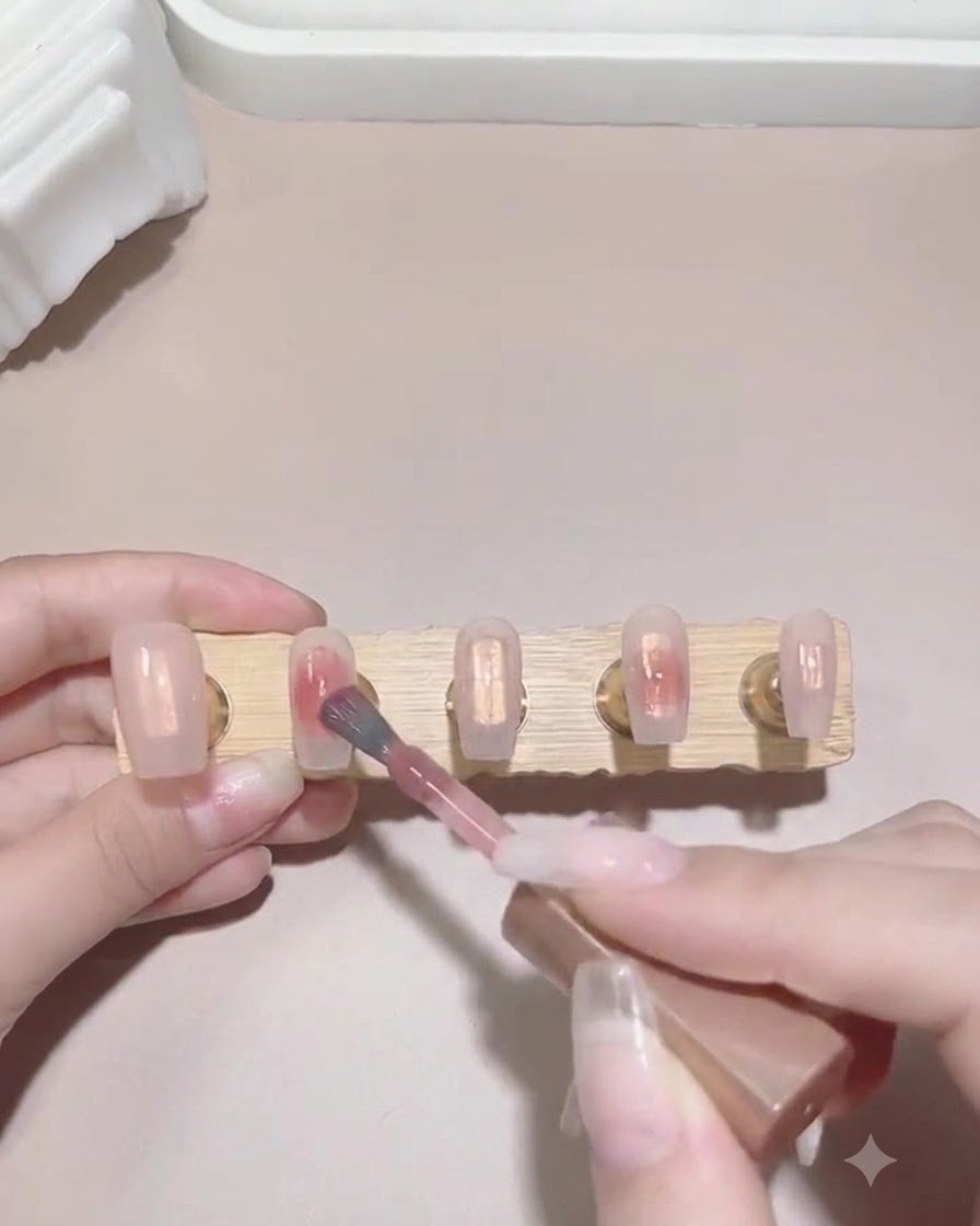Un pennello tampona una piccola goccia di smalto gel rosa sulla superficie bagnata dellunghia per avviare leffetto sfumato.