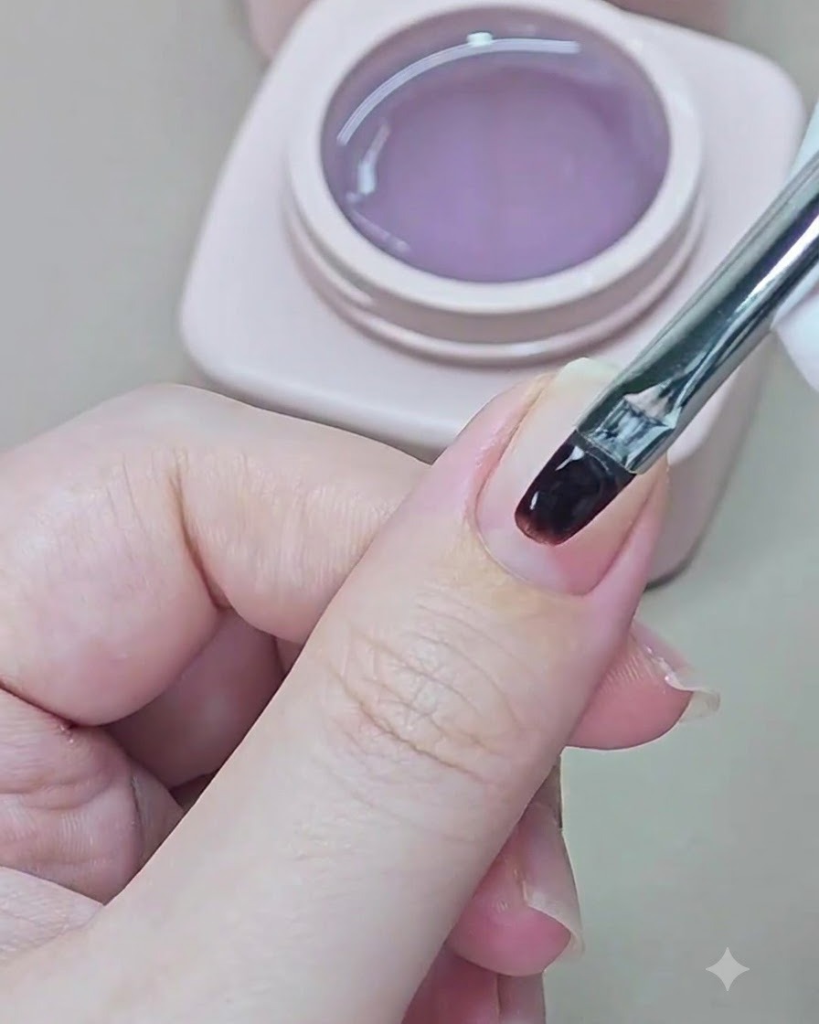 Un piccolo pennello per unghie applica il gel base trasparente su ununghia naturale.