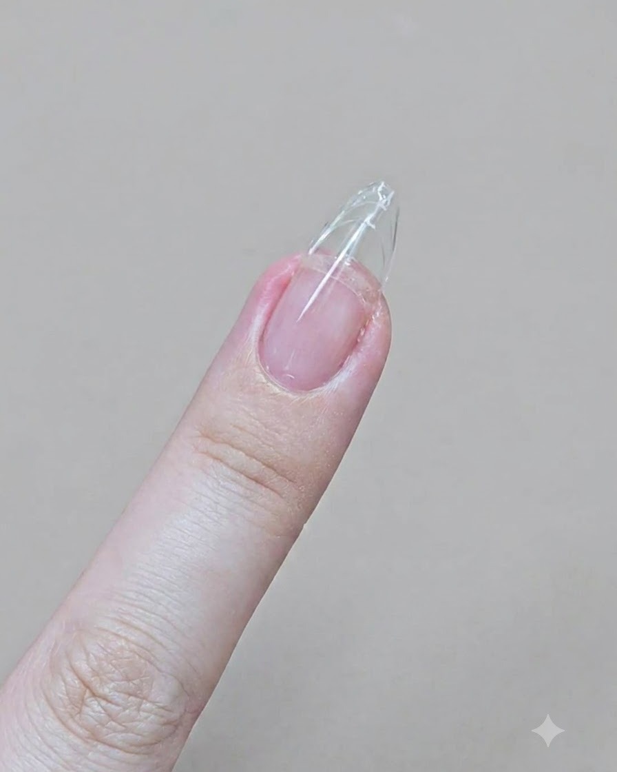 Un dito con unextension in gel trasparente viene limato in una forma a mandorla affilata con una lima in cartone.