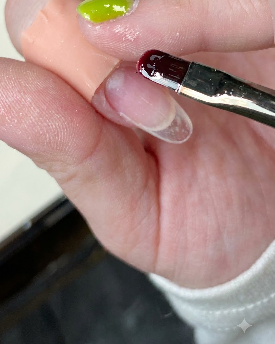 Un primo piano di un pennello da unghie che applica la base coat trasparente su una tip.