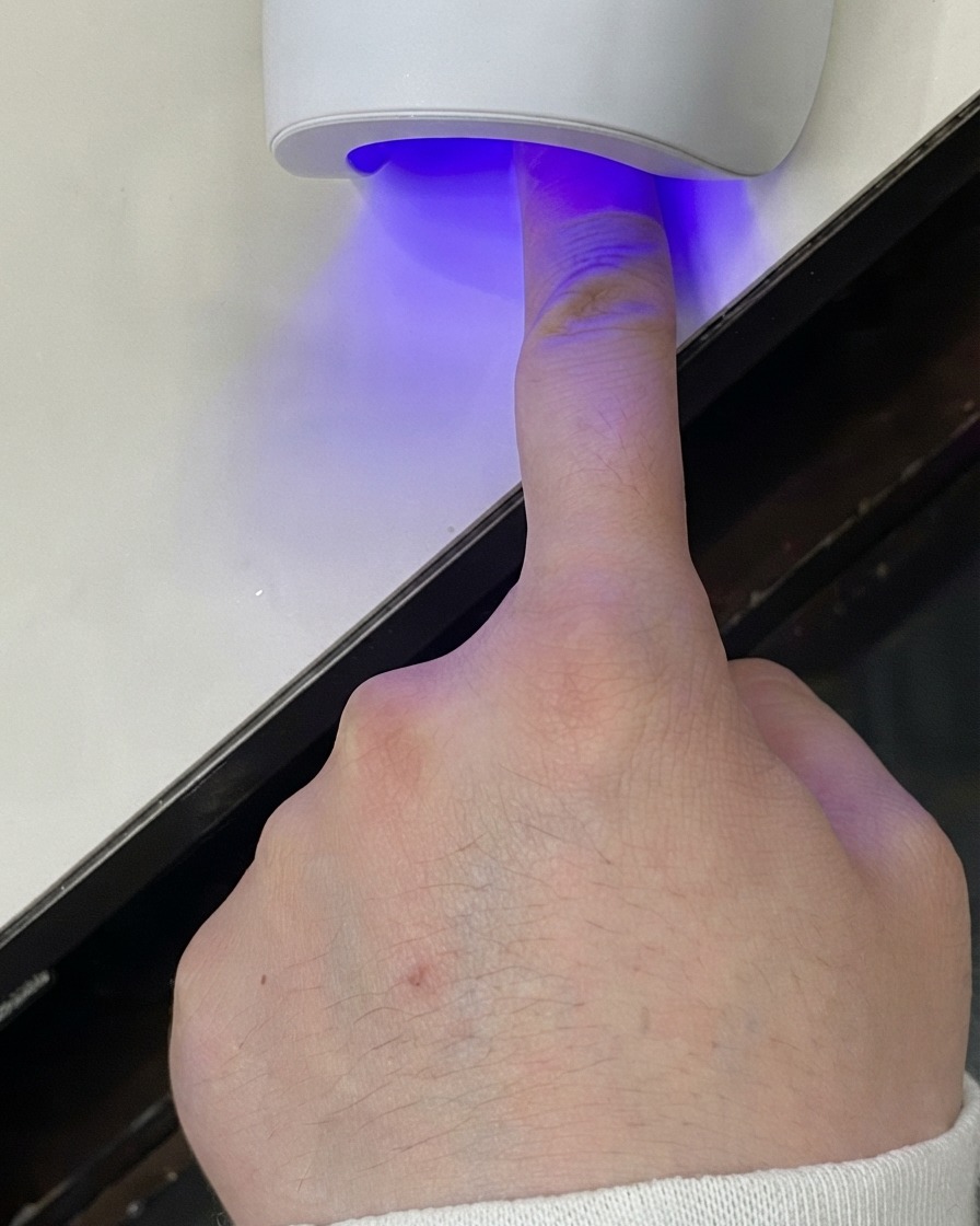 Un dito posizionato sotto una mini lampada UV LED per polimerizzare lo strato di gel.