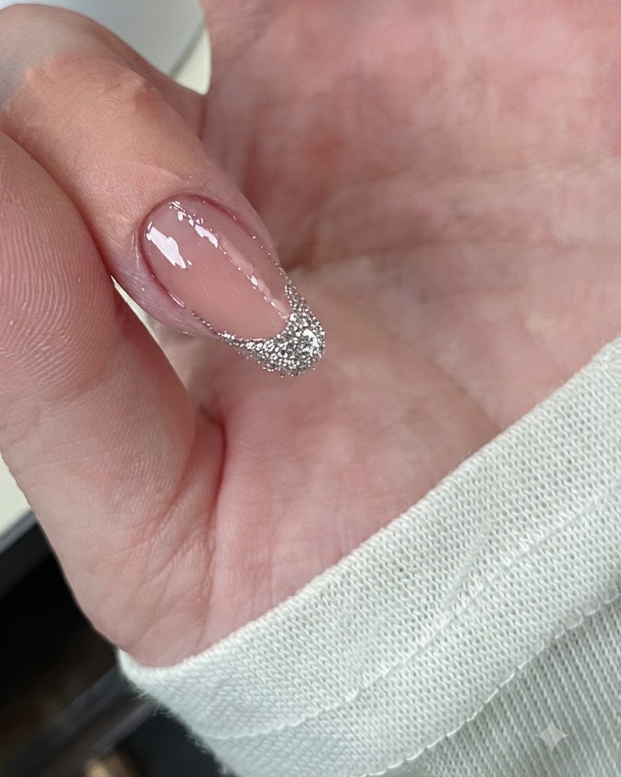 Un primo piano di ununghia che mostra glitter argento chunky stratificati densamente sulla french tip.