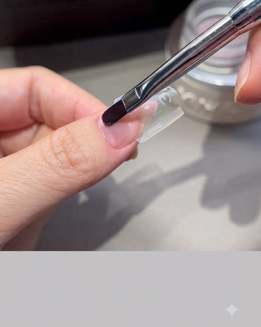 Un pennello professionale da unghie che distribuisce il gel di allungamento su uno stampo trasparente posizionato su un dito.