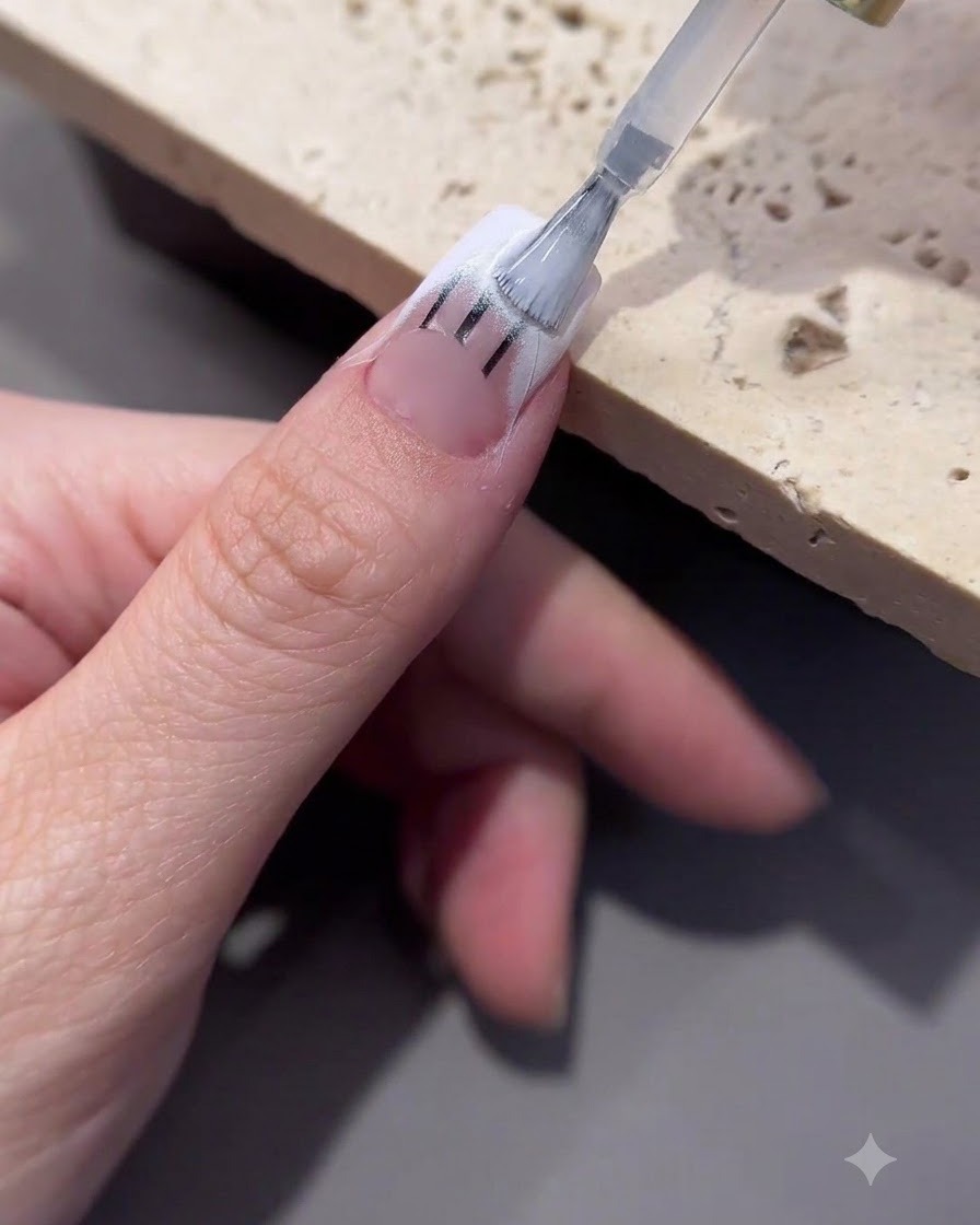 Un pennello che applica il gel di trasferimento sullarea della punta di ununghia decorata.