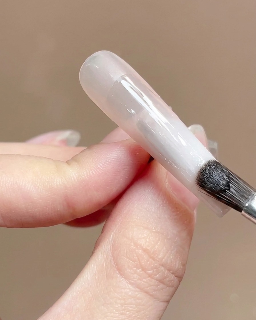 Un pennello per unghie che applica un top coat trasparente e lucido su una superficie di unghia sfumata.