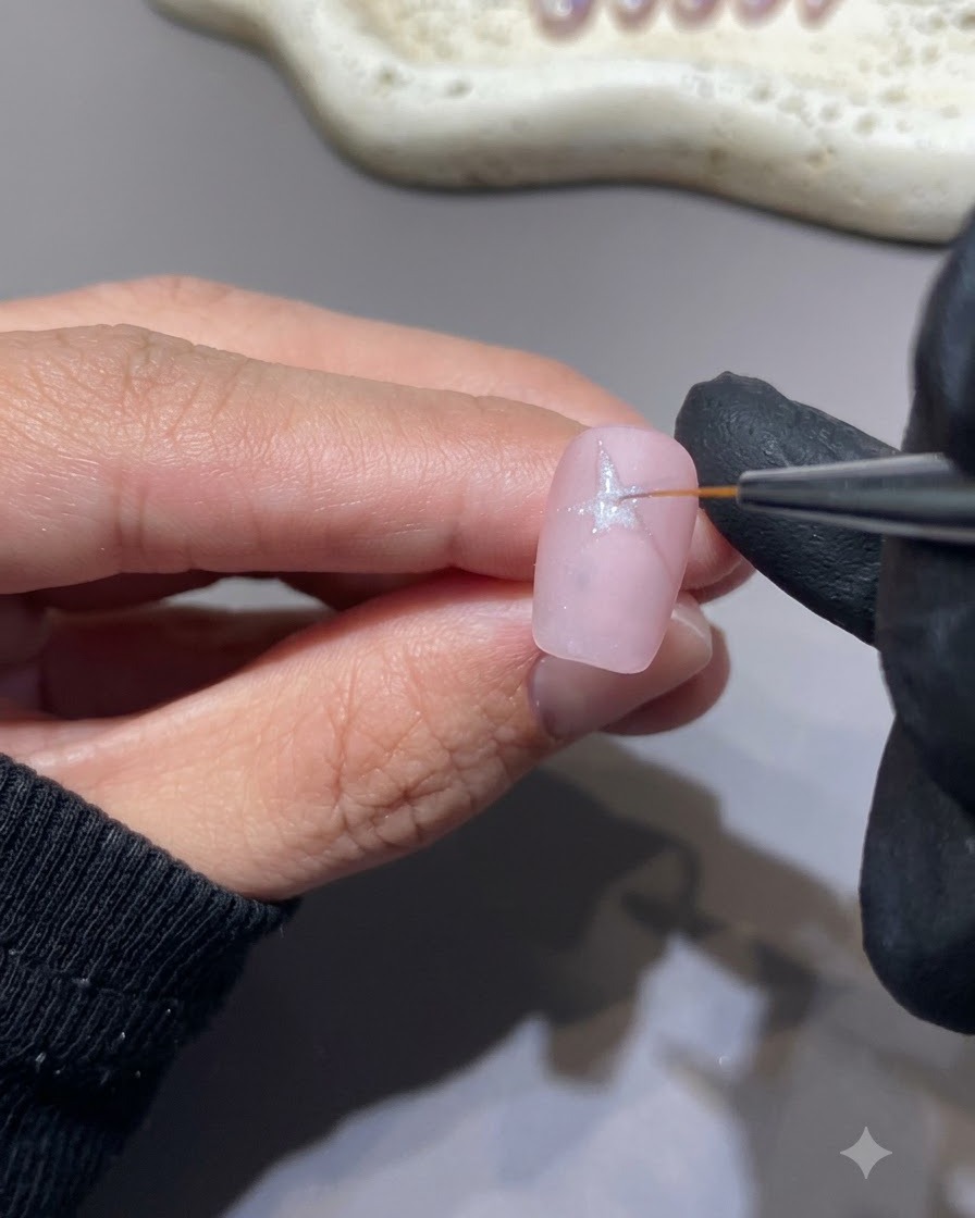 Un pennello a punta fine che disegna una stella bianca sulla superficie di ununghia rosa.