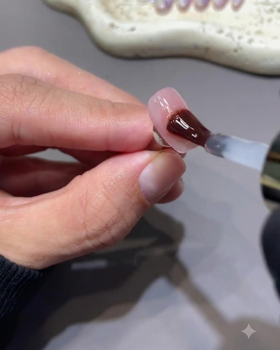 Un pennello che applica un top coat in gel lucido senza dispersione su ununghia con decorazione di stelle rosa bacca.