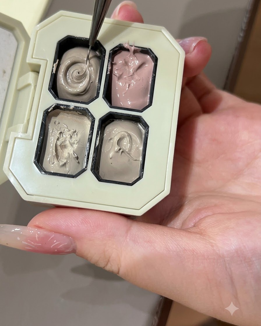Un pennello sottile per nail art che preleva gel colorato grigio da uno scomparto di una tavolozza.