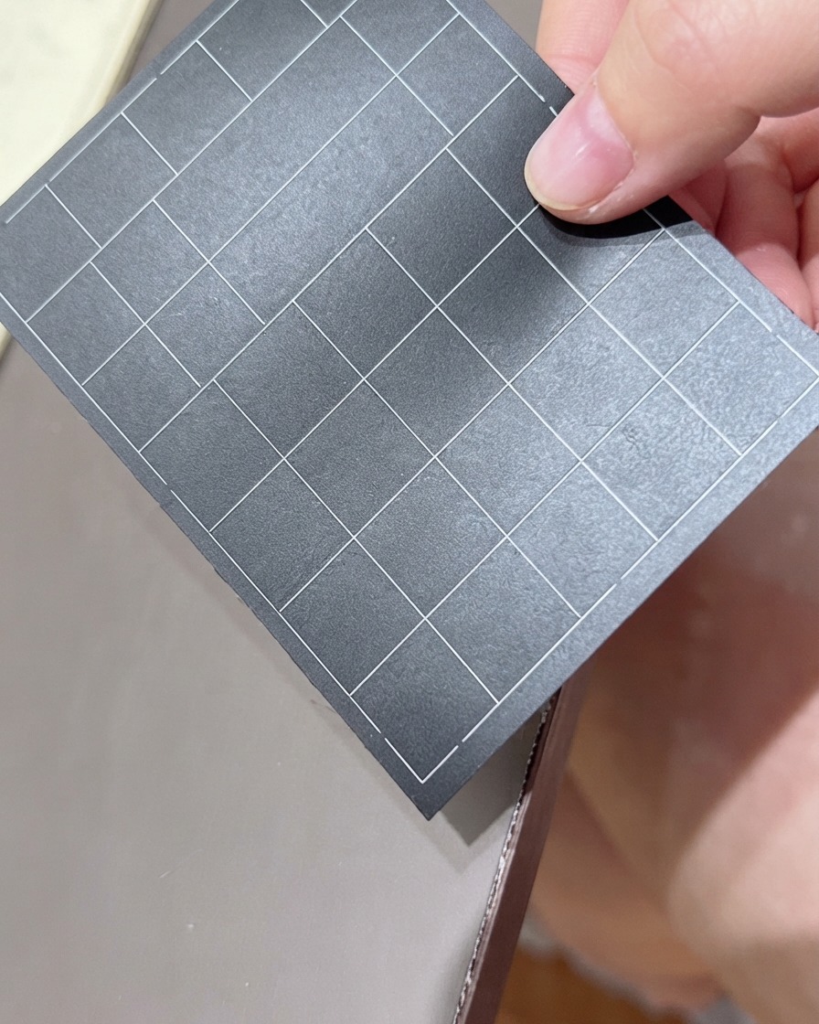 Una mano che regge un foglio nero di adesivi per unghie con griglia, selezionando un adesivo.