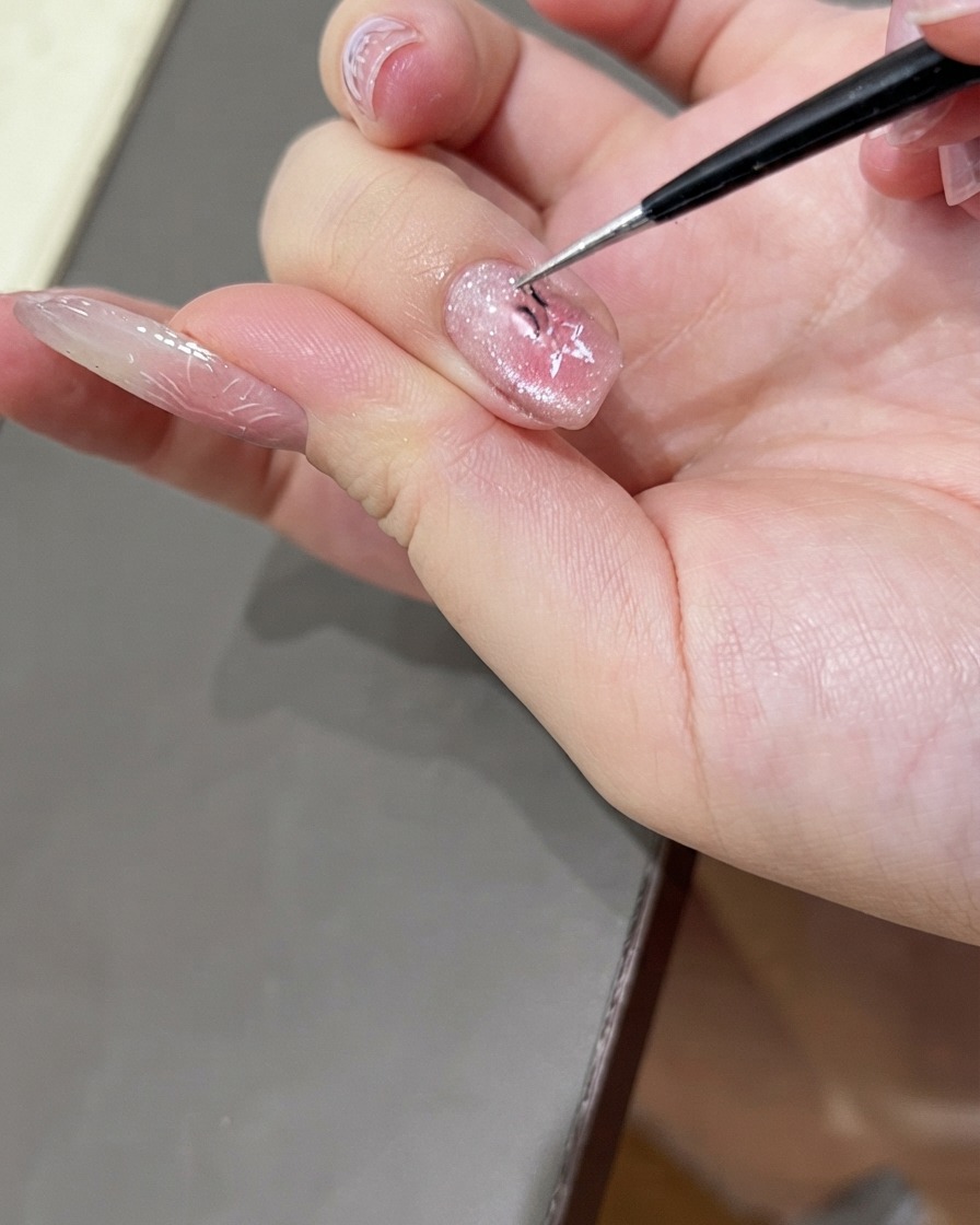 Un paio di pinzette sottili che rimuovono delicatamente un adesivo per unghie a forma di stella da ununghia decorata con gel cat-eye lucido.