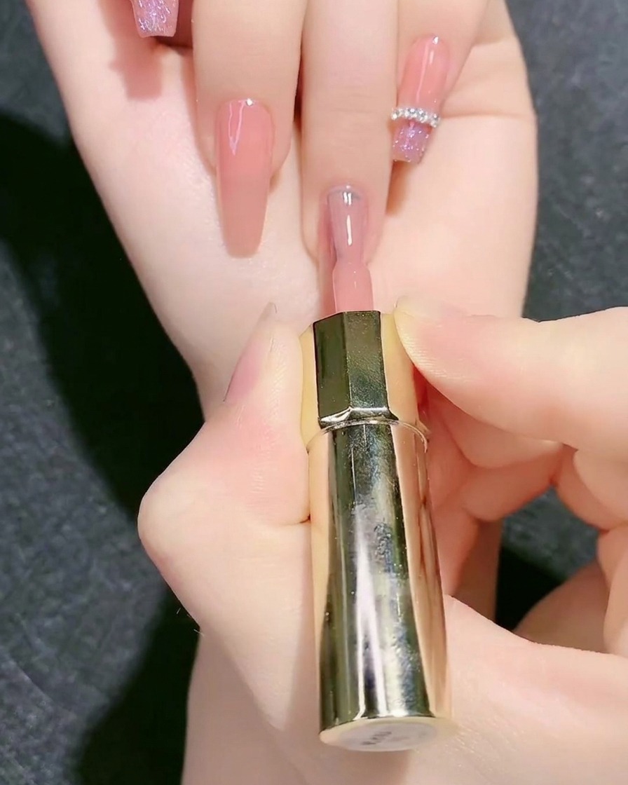 Un pennello da smalto applica il colore gel base rosa nudo su ununghia.