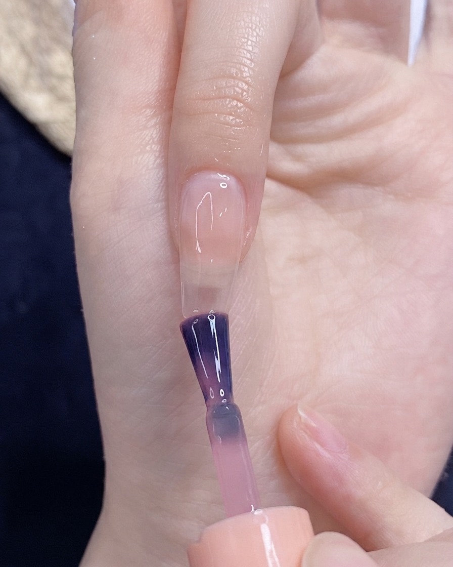 Un pennello che applica lo smalto gel rosa traslucido su ununghia naturale.