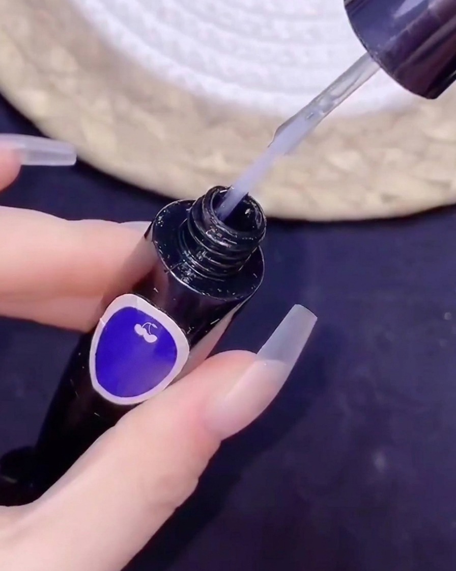Un pennello fine che intinge in un flacone di top coat no-wipe durante una procedura di nail art.
