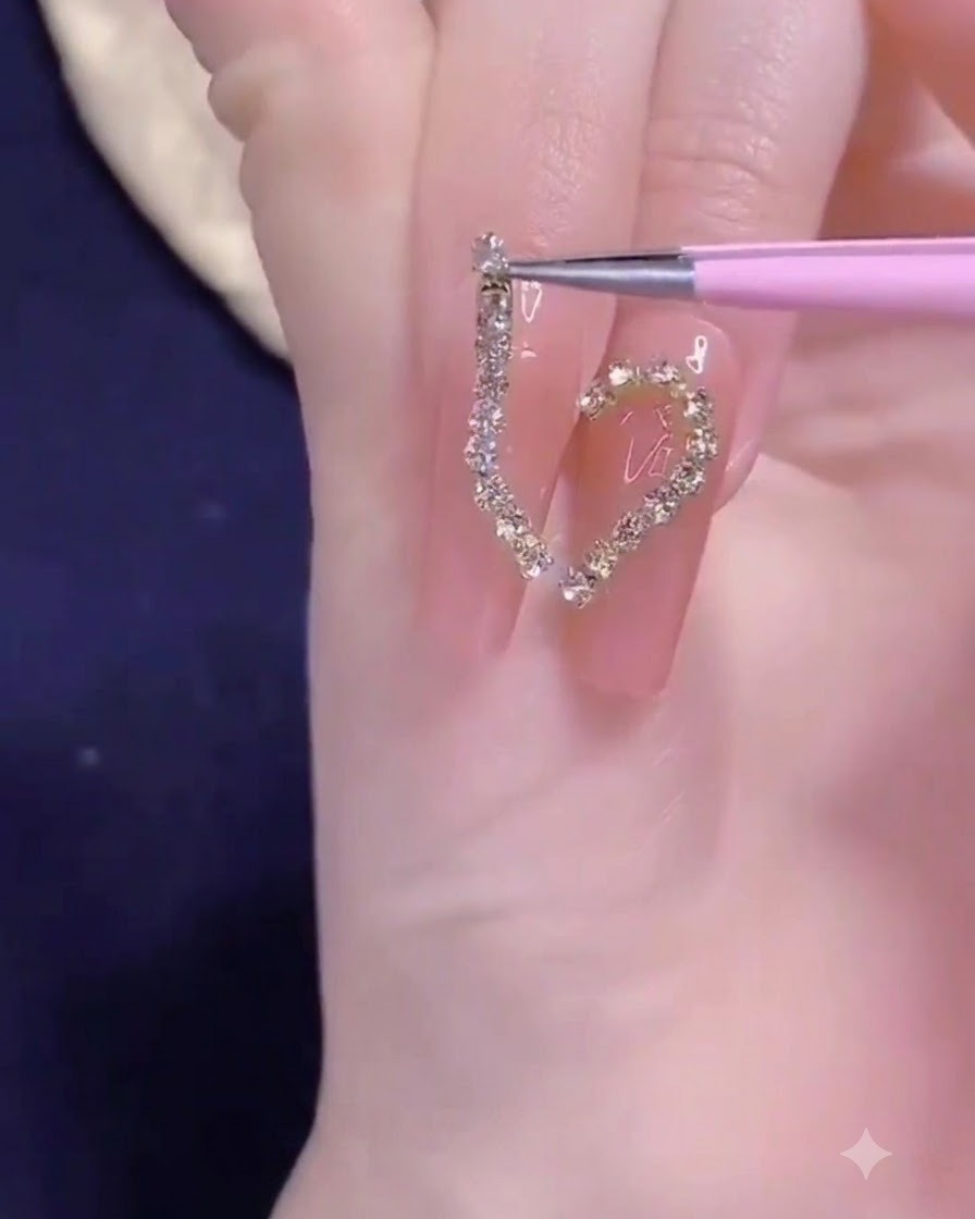 Una pinzetta di precisione che posiziona una striscia di catenella dorata sul design a mezzo cuore dellunghia.