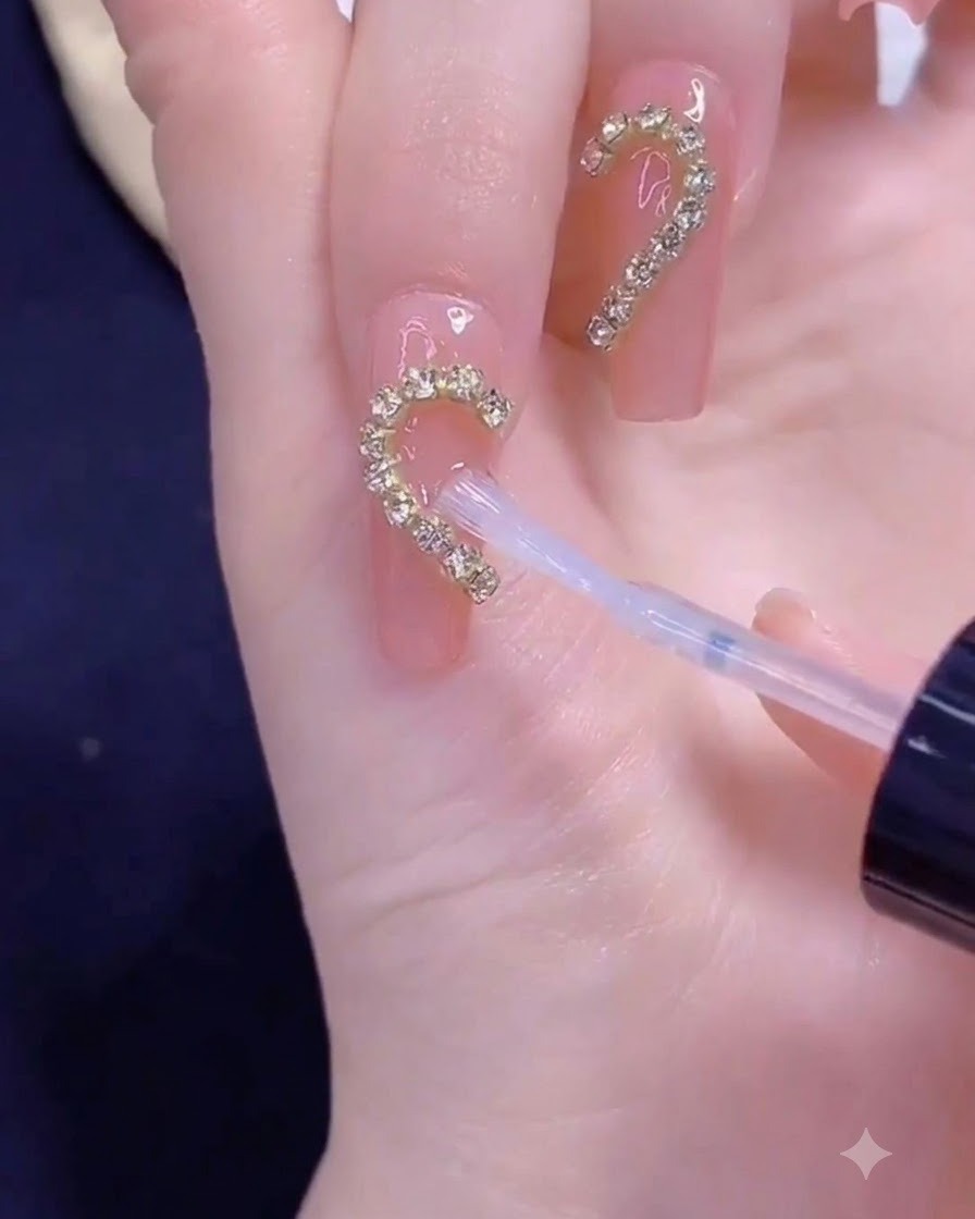 Un pennello che applica il top coat trasparente su una striscia di catenella dorata disposta a forma di mezzo cuore su ununghia.