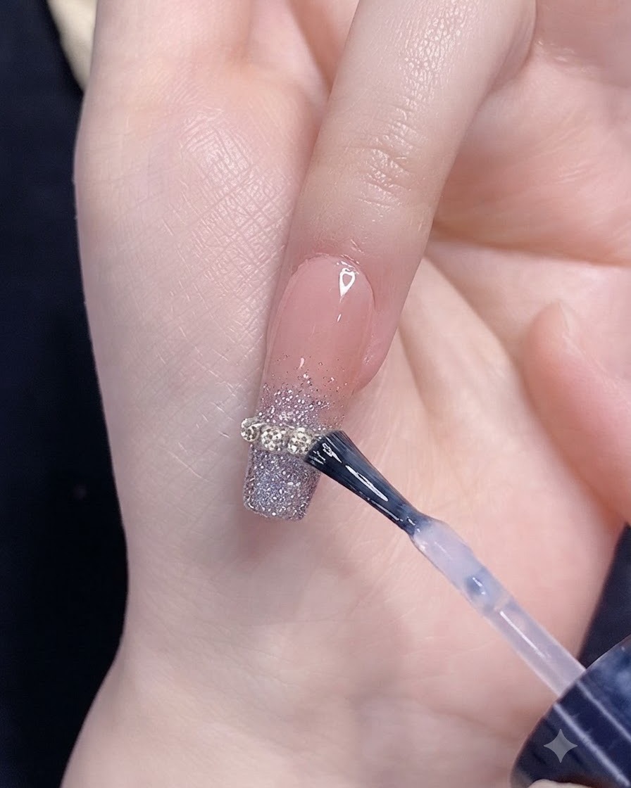 Un pennello che applica il top coat su ununghia con sfumatura di glitter argentati e un accento in catenella.