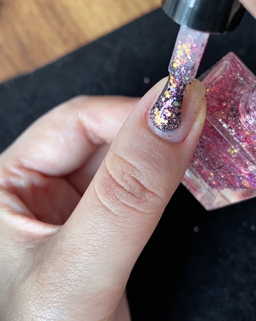 Una vista ravvicinata di ununghia naturale con uno strato base nudo e poche scaglie di glitter sparse.