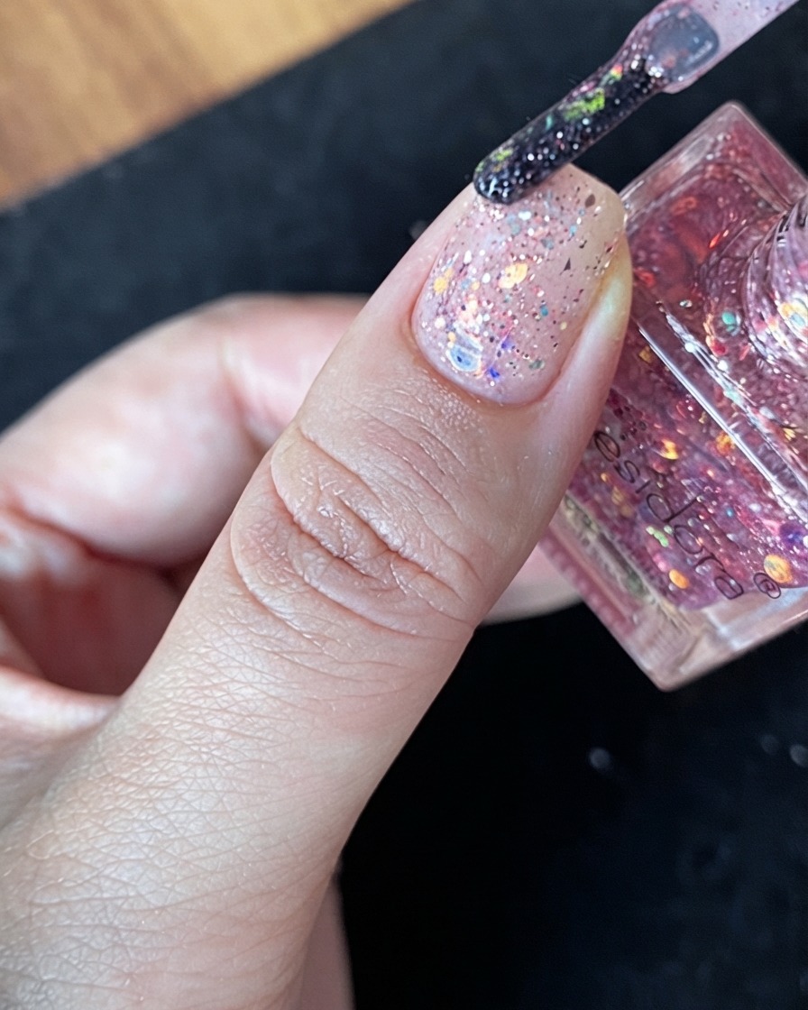 Un abbondante gruppo di scaglie di glitter multicolore posizionato direttamente al centro di ununghia nudo.
