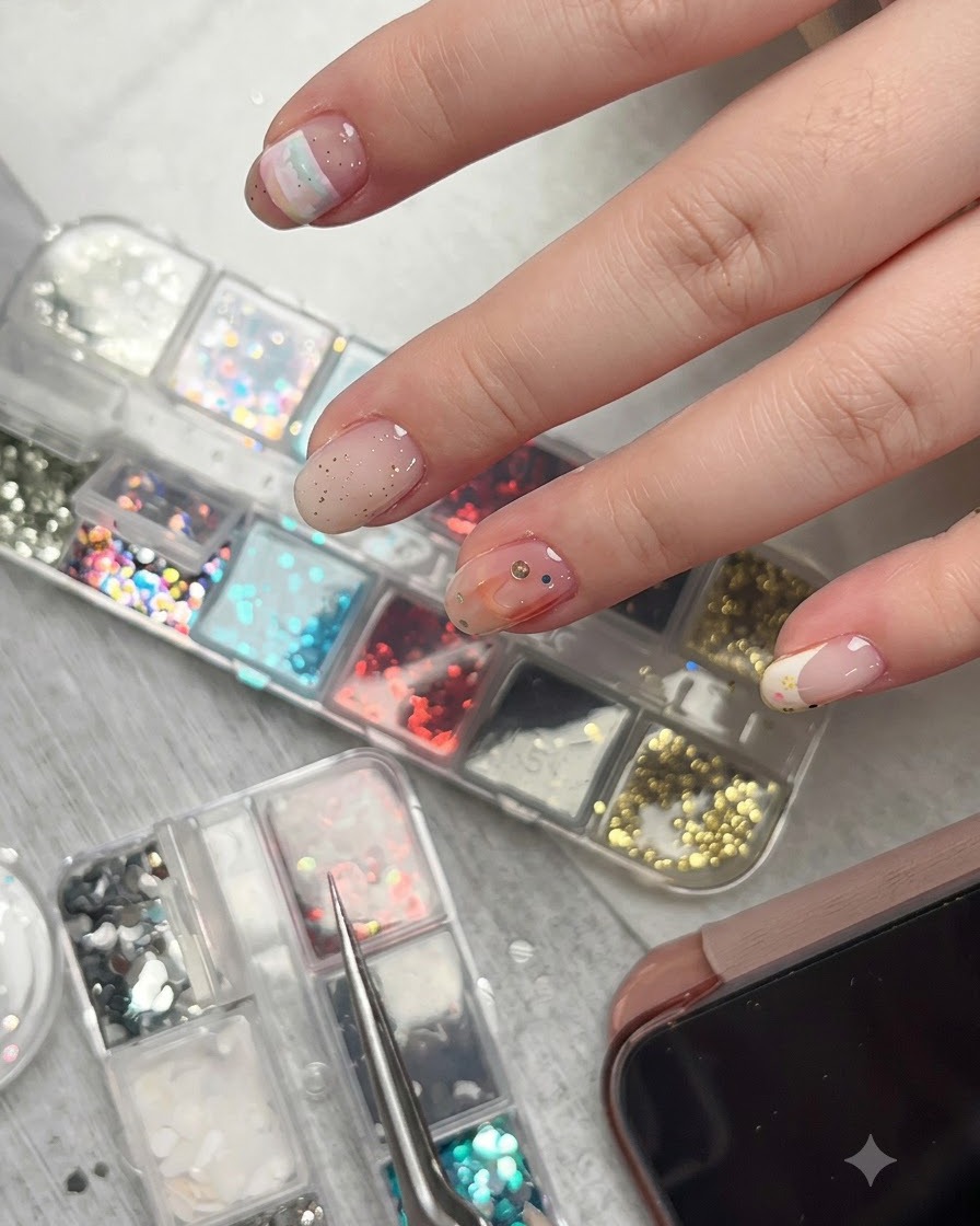 Un paio di pinzette che tengono un minuscolo pezzo di glitter a stella appena sopra la superficie di ununghia decorata con vari accenti.