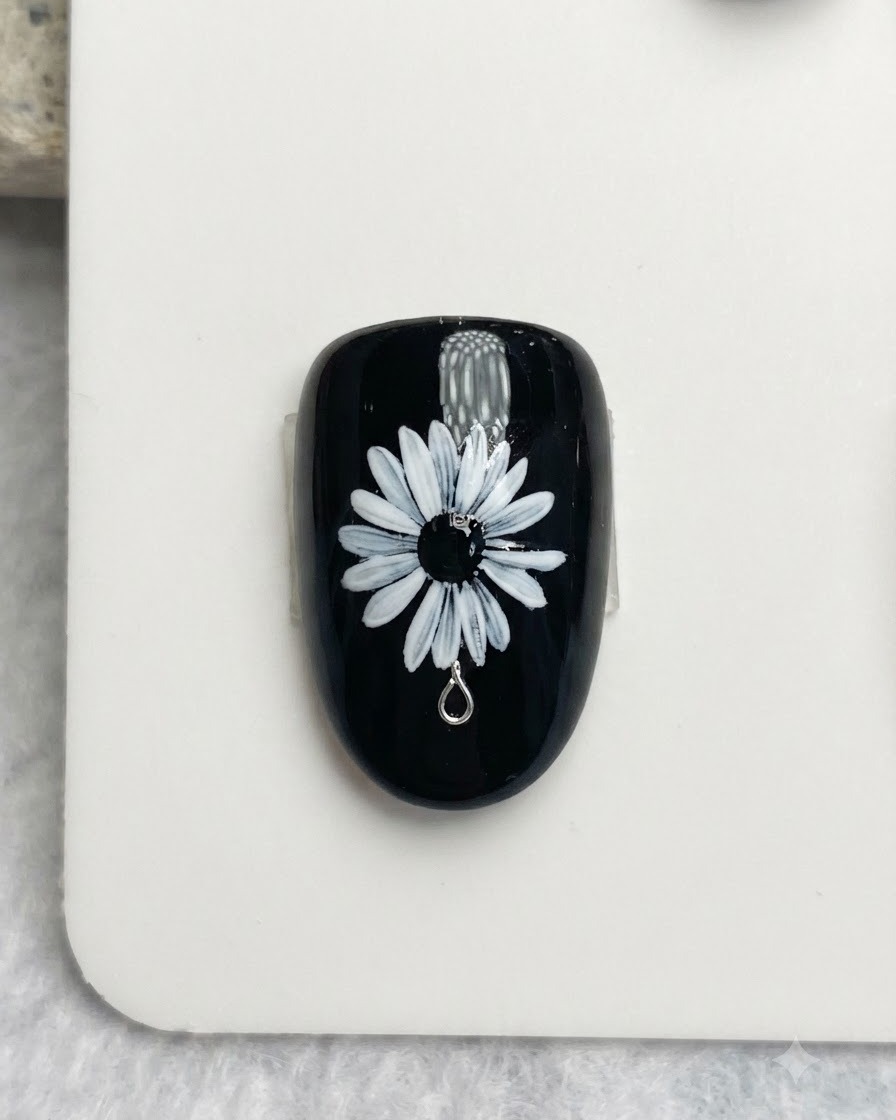 Primo piano di un pennello da unghie che dipinge delicati punti bianchi e gialli al centro nero di una nail art con margherita bianca.