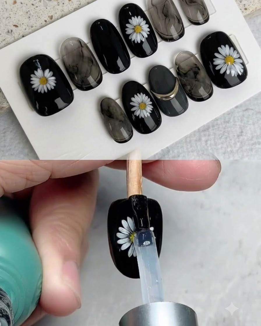 Un pennello che applica un top coat lucido su ununghia nera finita decorata con una margherita bianca.