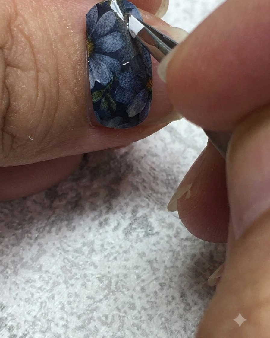 Un pennello liner sottile dipinge con cura gel bianco sui petali di una margherita su ununghia grigia.