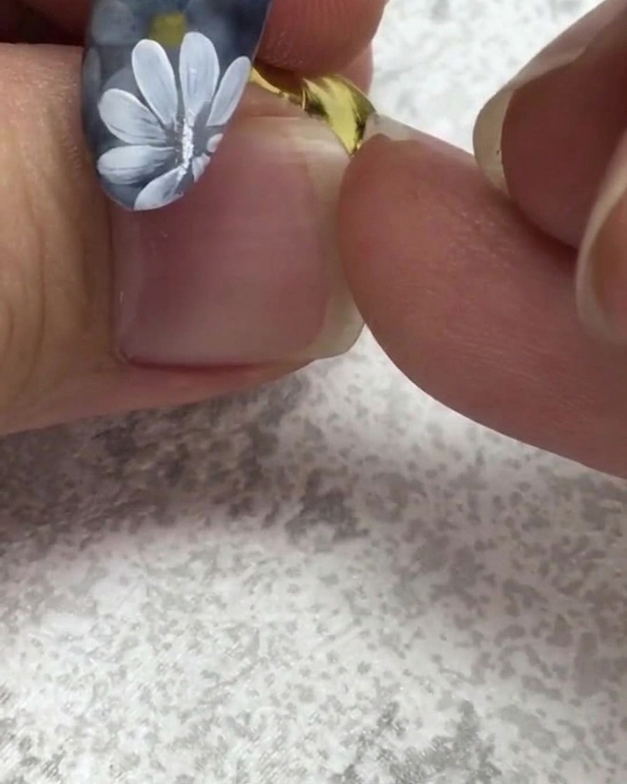 Un pennello per unghie piatto raccoglie un piccolo punto di gel verde vicino a ununghia con margherite bianche.