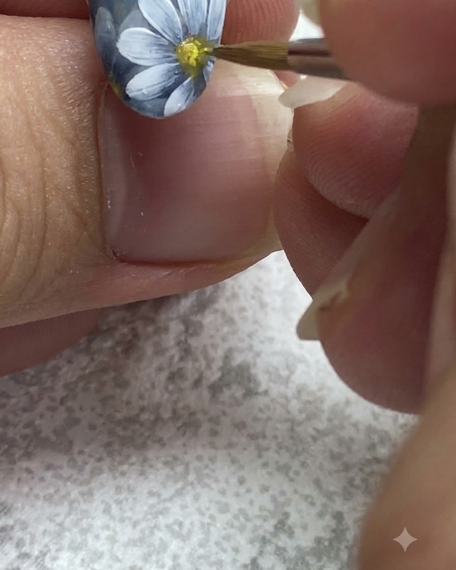 Un pennello fine tampona gel giallo nel centro di una margherita bianca dipinta.