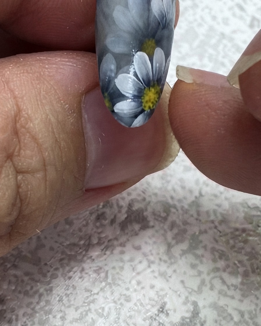 Un pennello liner fine aggiunge una seconda foglia verde allangolo superiore di un design per unghie floreale.