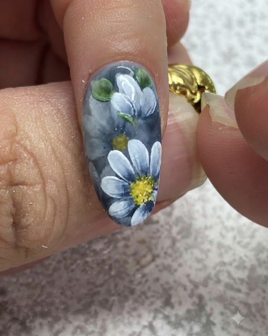 Un pennello fine aggiunge punti luce dettagliati su foglie verdi dipinte su una manicure in gel grigio.