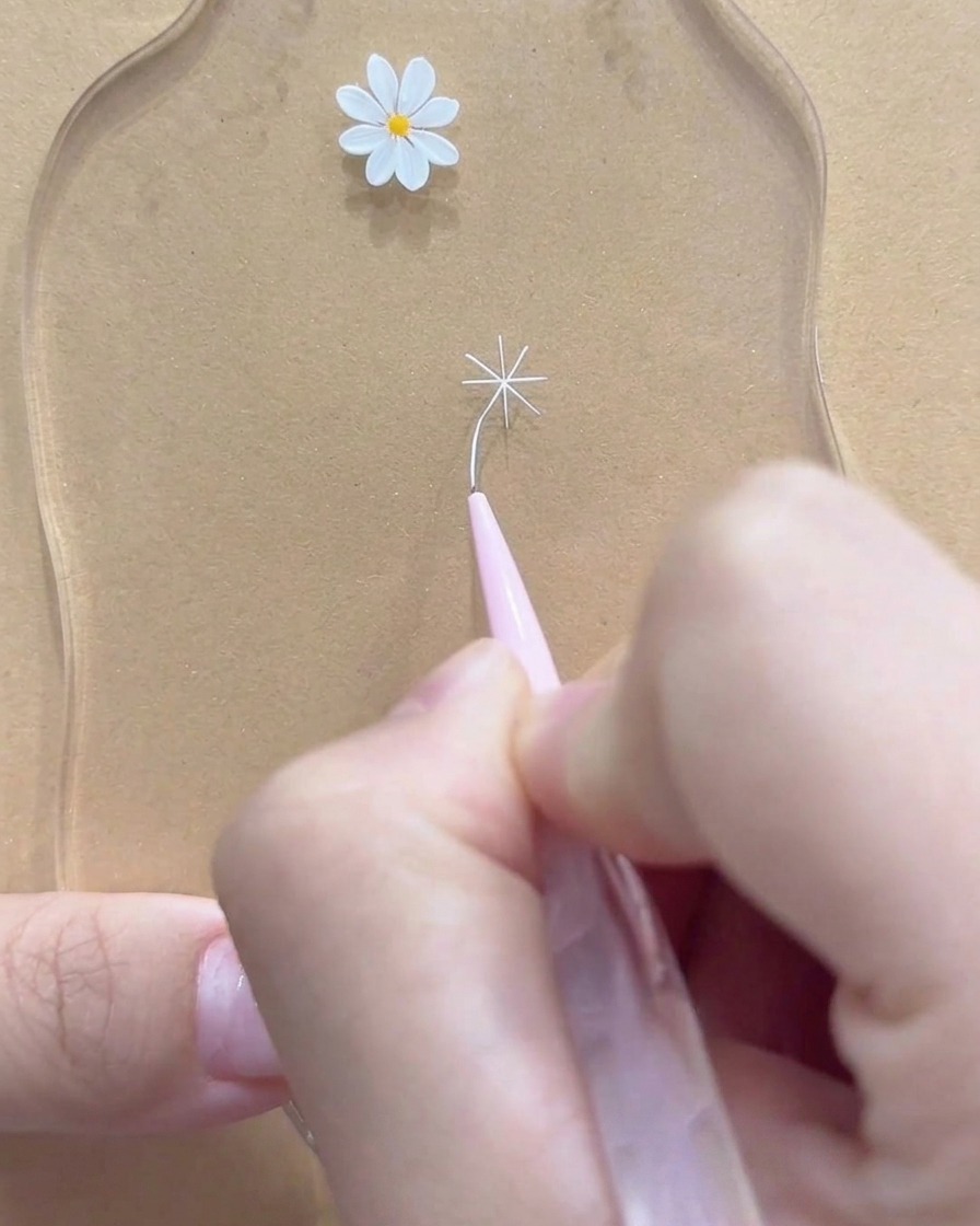 Un primo piano di un pennello a punta fine che perfeziona le punte esterne di un fiore di margherita bianco.