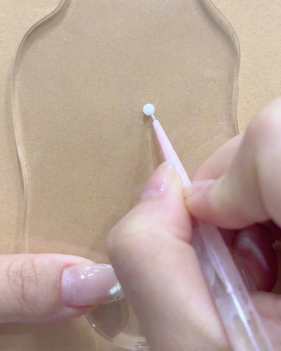Un dotting tool o un pennello poggiato vicino a un punto pulito sulla tavolozza acrilica trasparente.