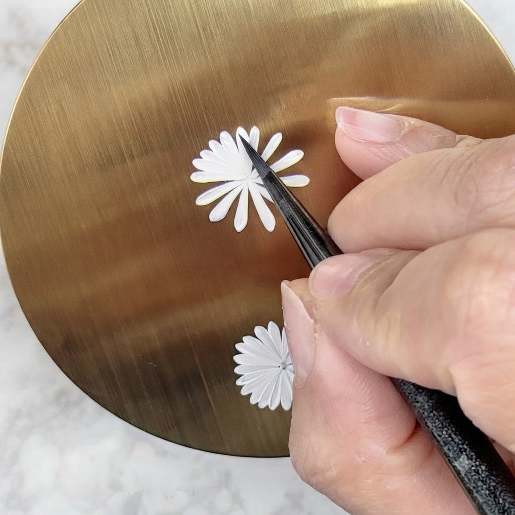 Un pennello per nail art che dipinge attentamente un secondo strato interno più piccolo di petali bianchi su un design di margherita.