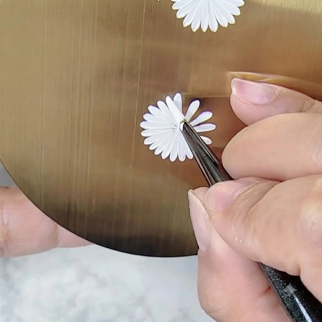 Una mano che tiene un pennello per nail art a un angolo regolato per dipingere i dettagli su un design di margherita senza ruotare troppo la tavolozza.